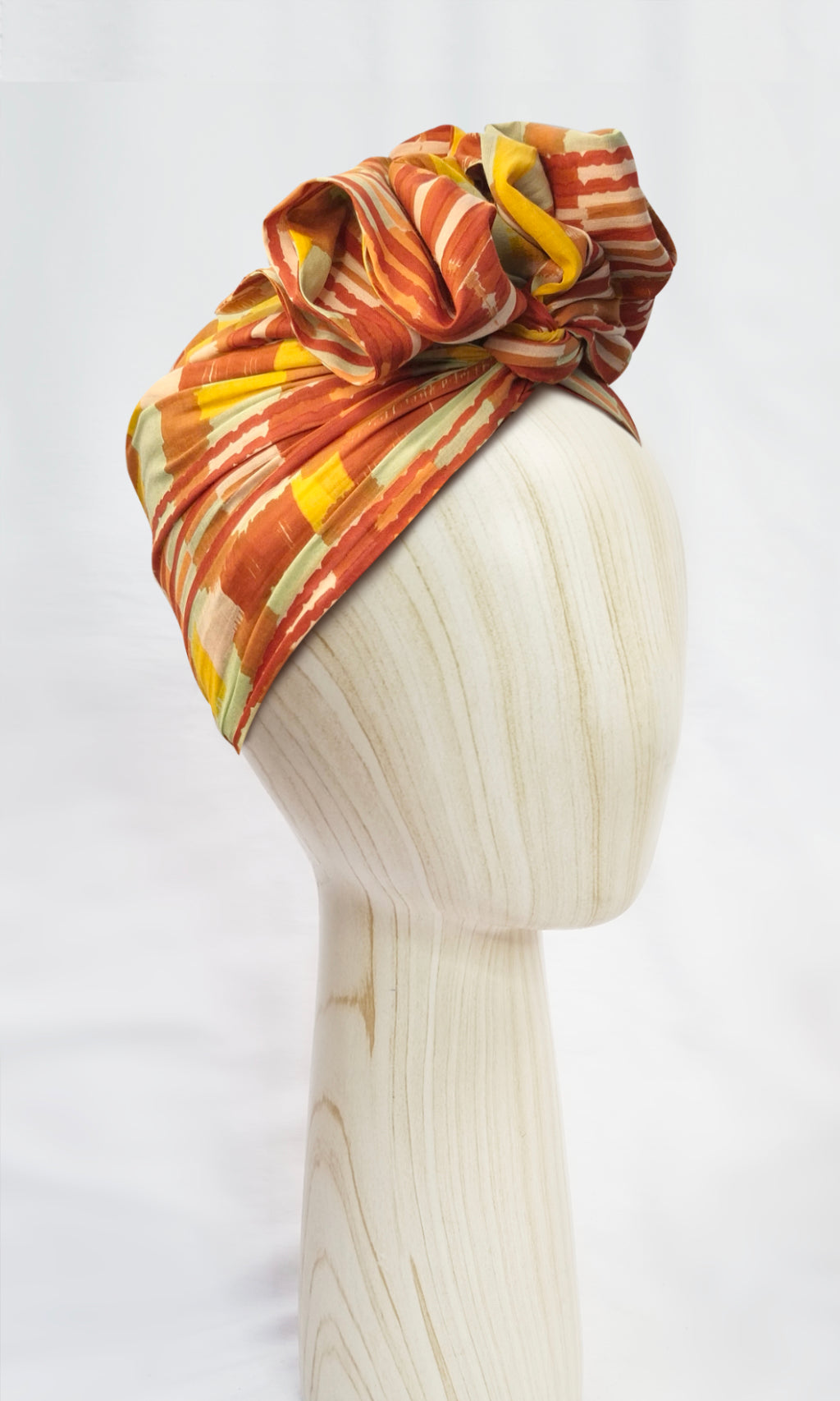 Side view of the Celine Martine Josephine Wired Head Wrap on display head, featuring earthy brushstroke pattern in orange, yellow and aqua
