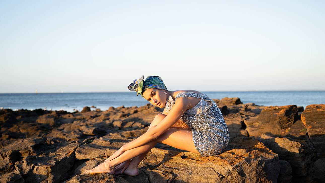 Céline Martine banner featuring a woman wearing stylish wired head wrap or comfortable chemo turban  sitting fashionably on rocky ocean coast