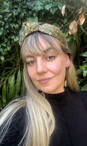 Woman wearing a Celine Martine top knot headband made in a green gold Sari with green foliage in the background